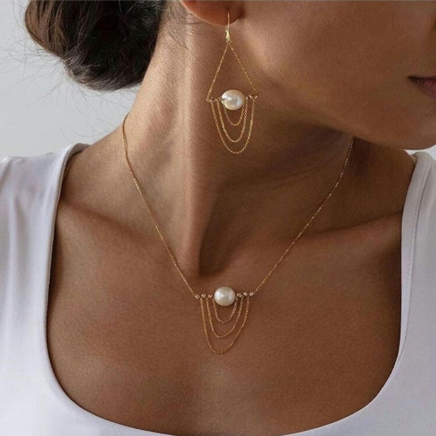 Gold necklace with pearl pendants worn by a person against a neutral background