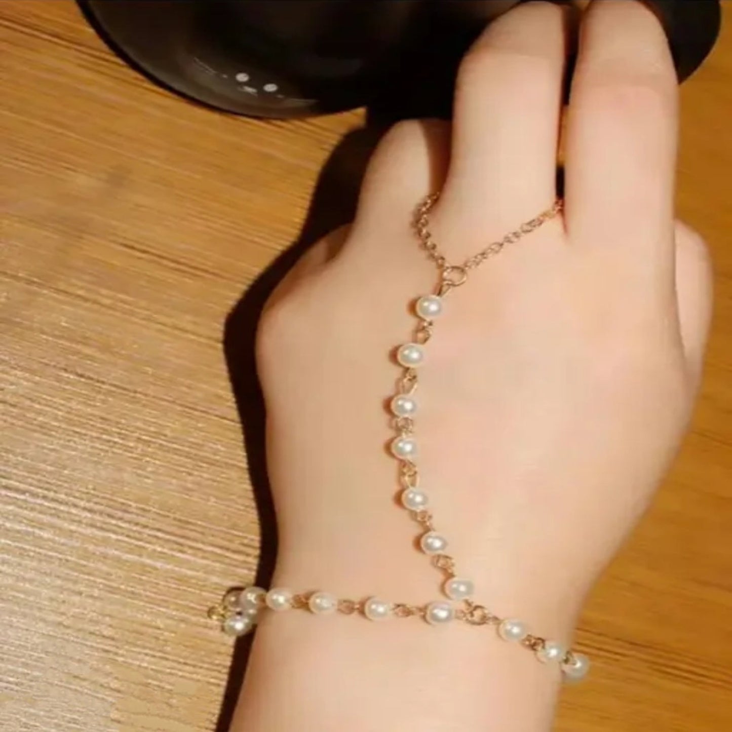Hand wearing a pearl bracelet on a wooden surface