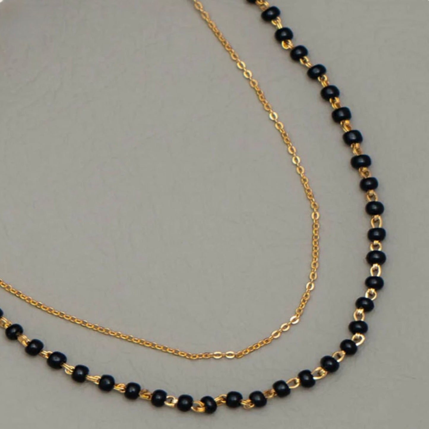 Two gold necklaces with black beads on a gray background