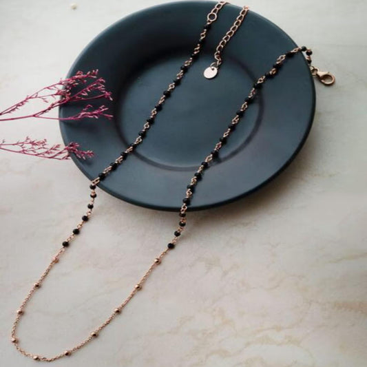 Necklace with black beads and rose gold chain on a dark plate