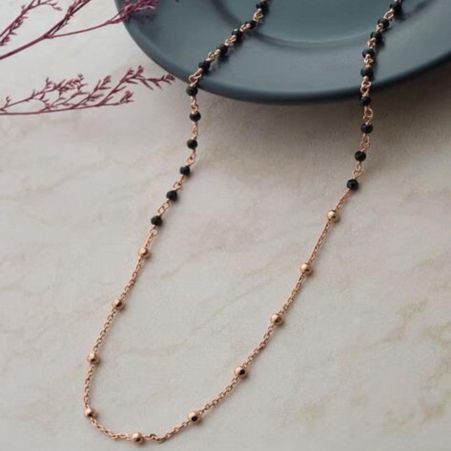 Rose gold necklace with black beads on a light surface