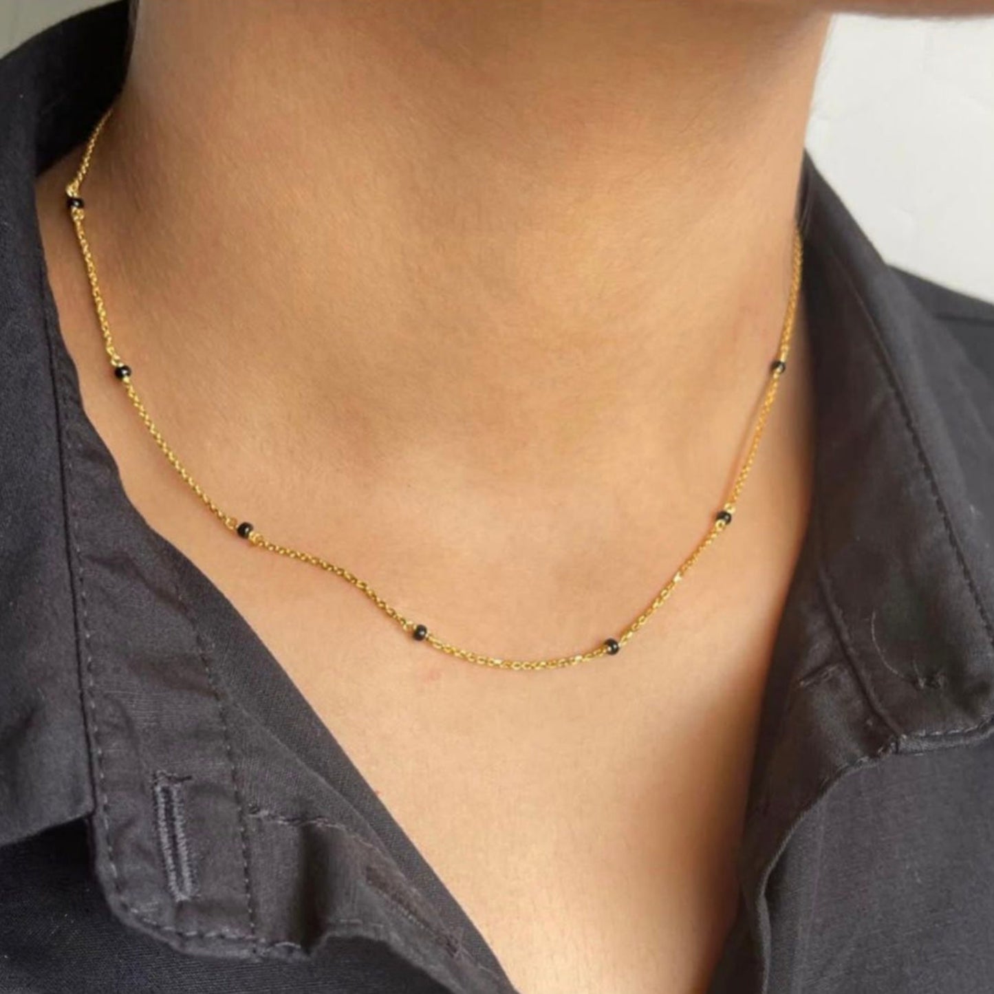 Gold necklace with small black beads worn by a person against a neutral background