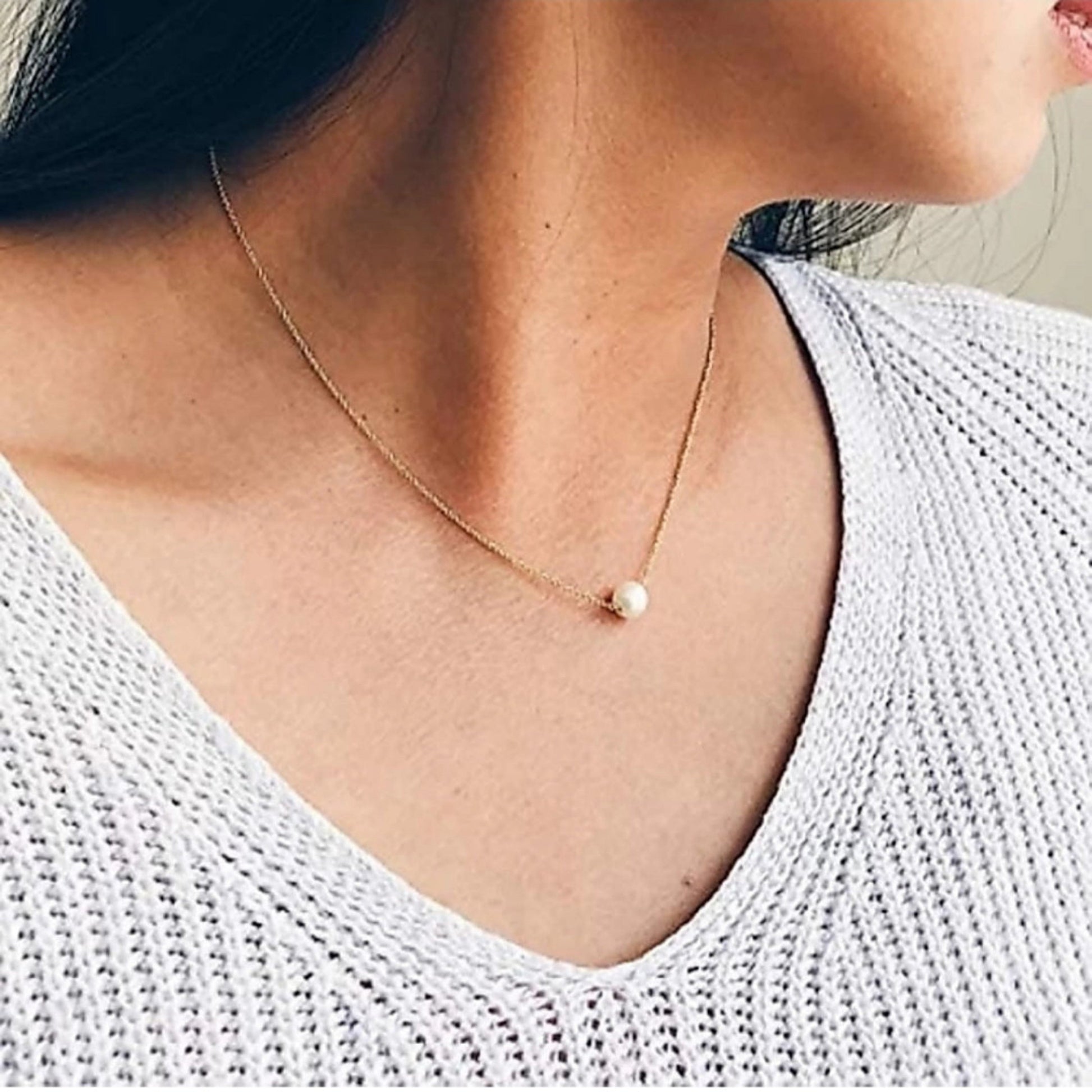 Close-up of a person wearing a delicate gold necklace with a small pearl pendant.