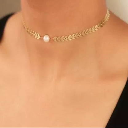 Gold necklace with a pearl pendant on a person wearing a black top.
