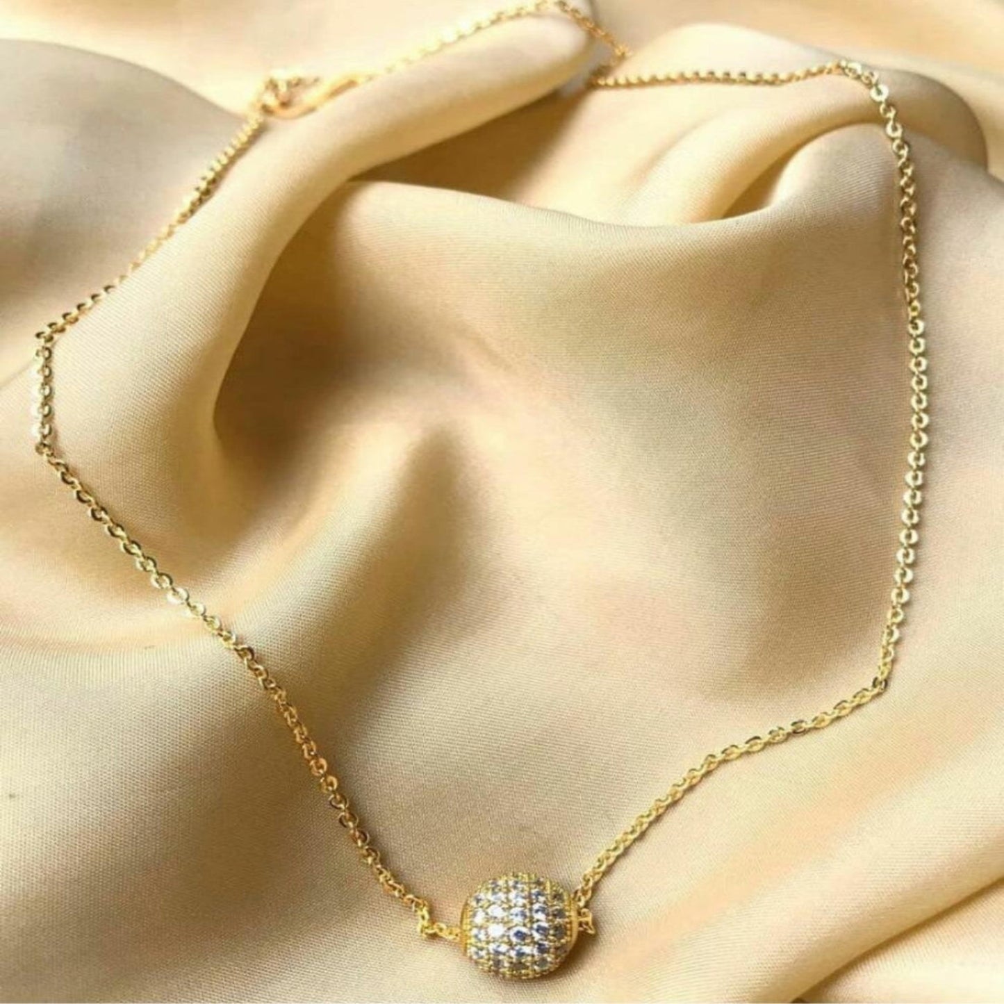Gold necklace with a sparkling pendant on a beige fabric background