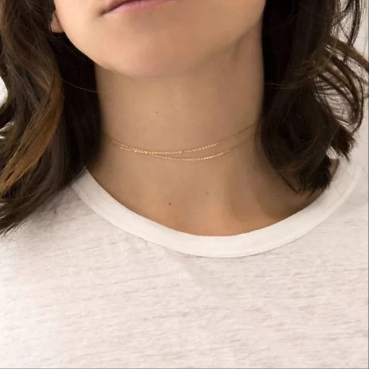 Close-up of a person wearing a delicate gold necklace on a plain background