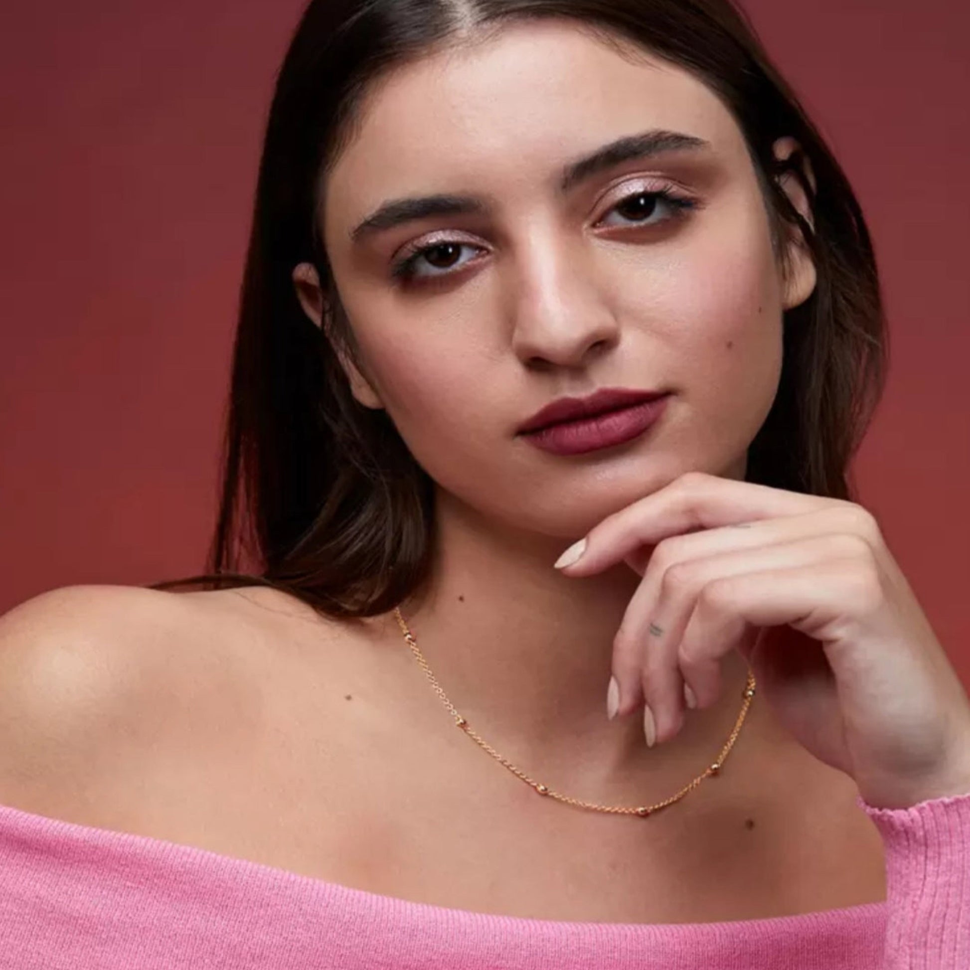 Woman wearing a gold necklace against a red background