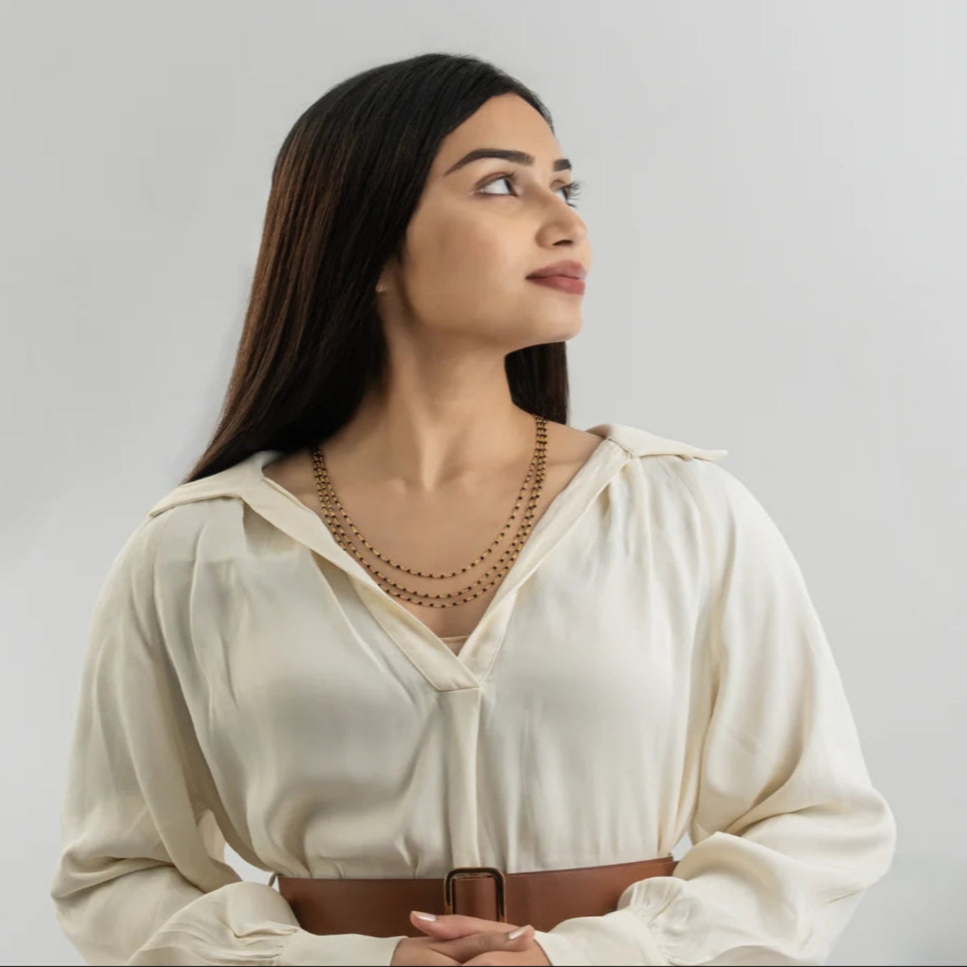 Woman wearing a white blouse with a brown belt against a plain background