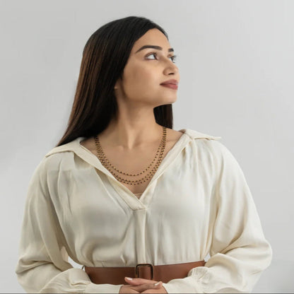 Woman wearing a white blouse with a brown belt against a plain background