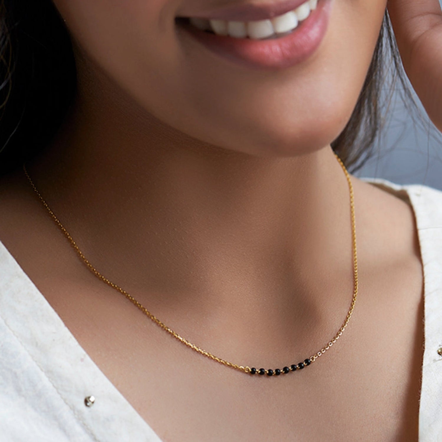 Close-up of a person wearing a gold necklace with black beads.