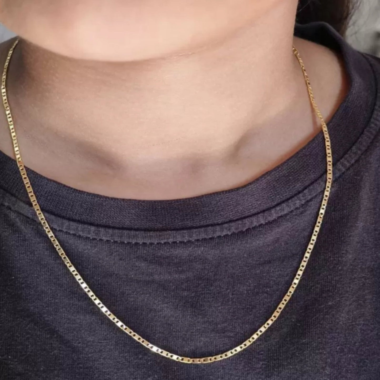 Gold chain necklace worn by a person on a plain background