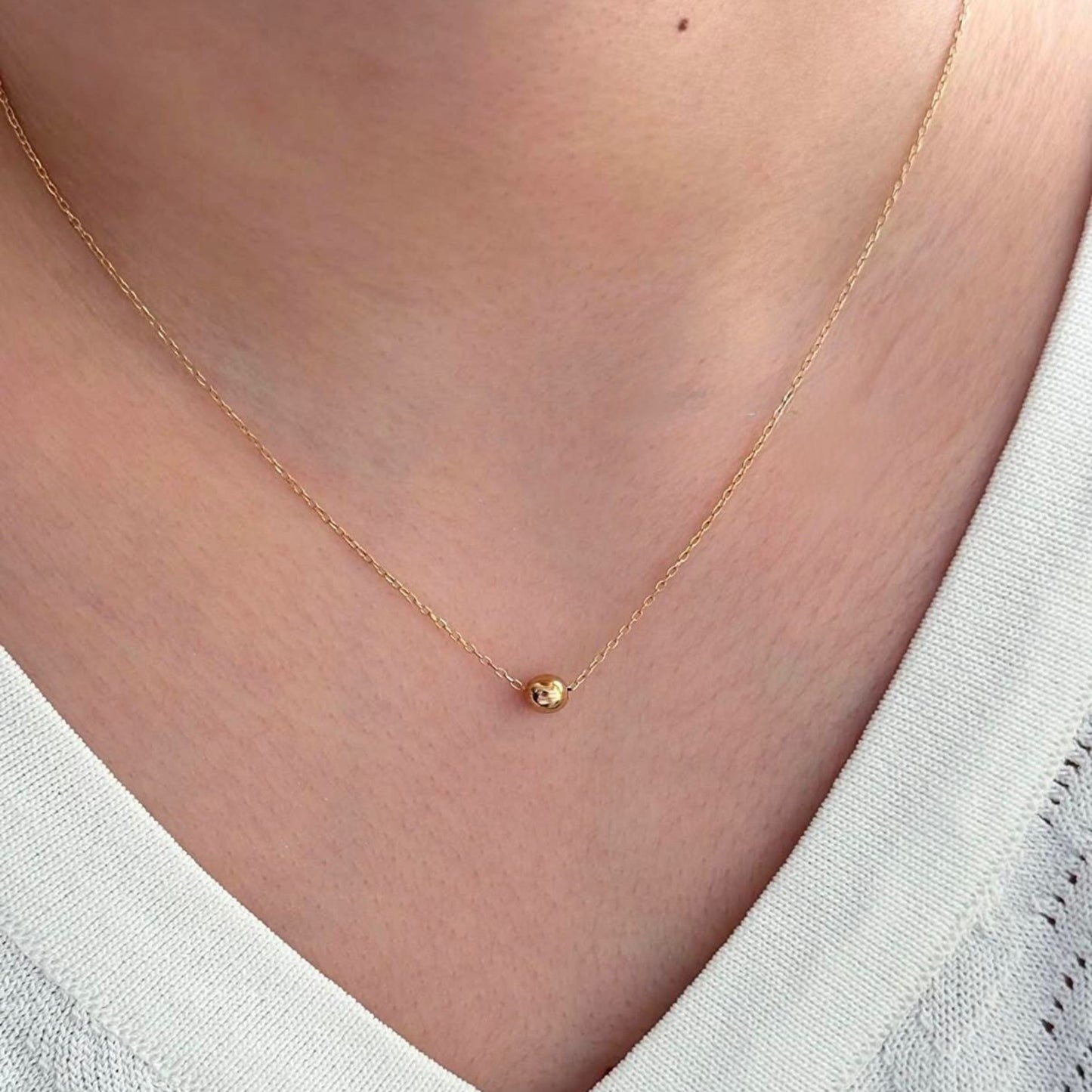Gold necklace with a small heart pendant on a person wearing a white top.
