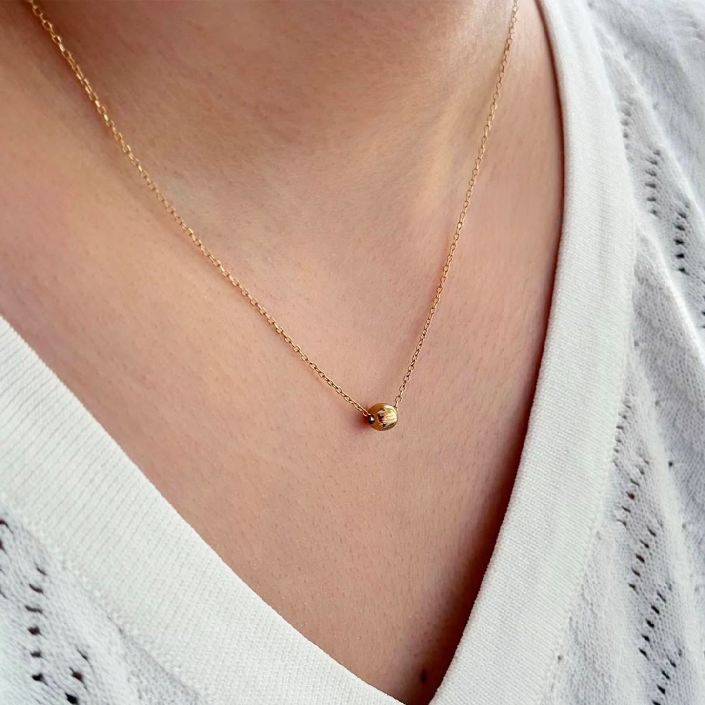 Gold necklace with a small pendant worn by a person in a white top
