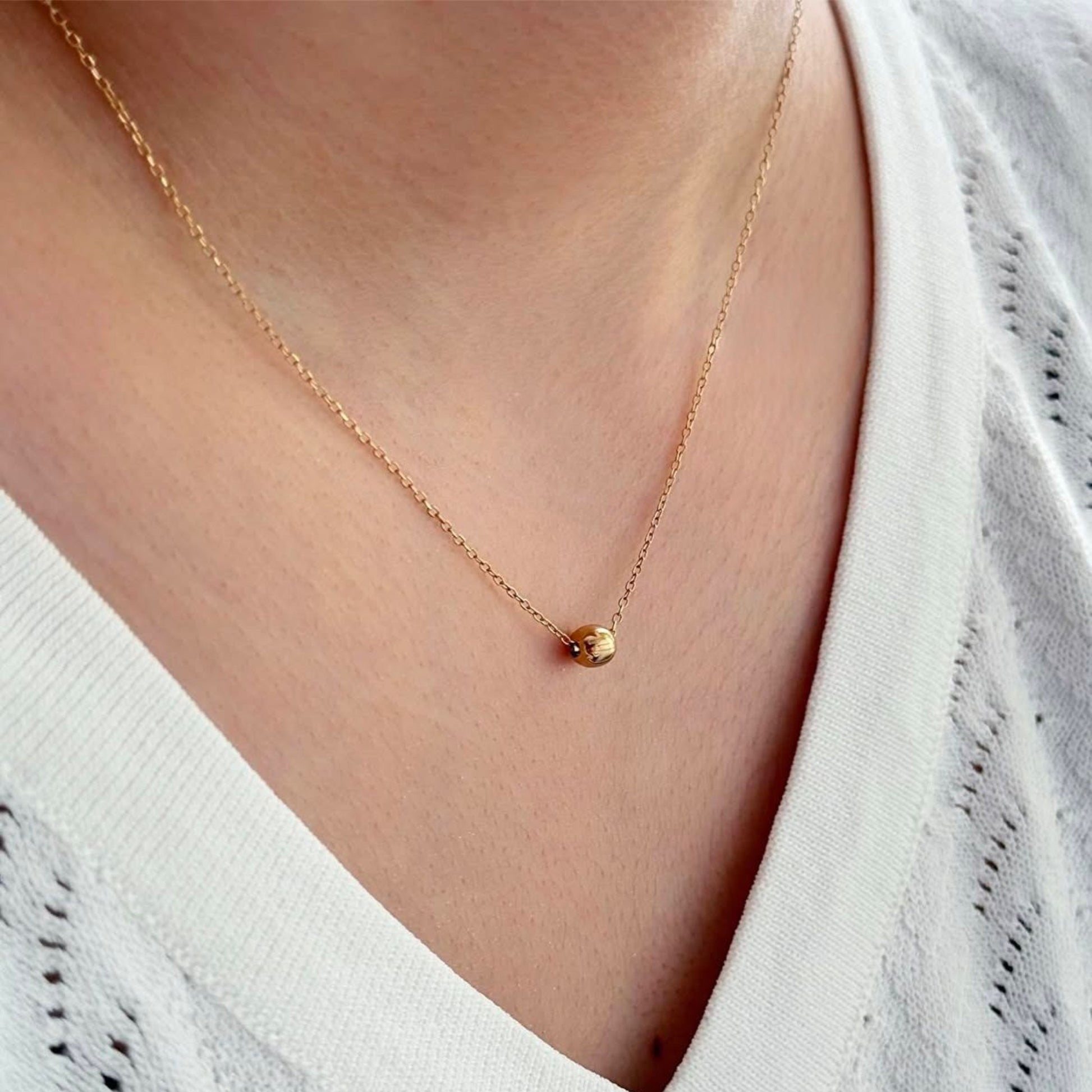 Gold necklace with a small pendant worn by a person in a white top