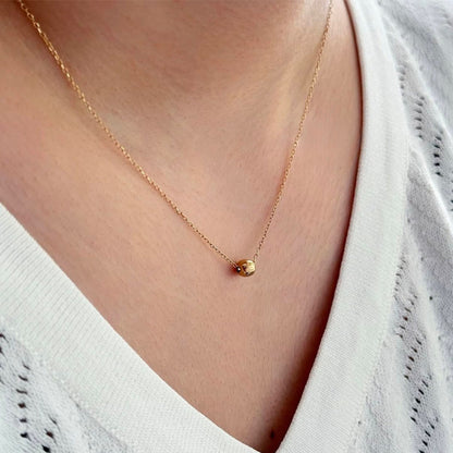 Gold necklace with a small pendant worn by a person in a white top