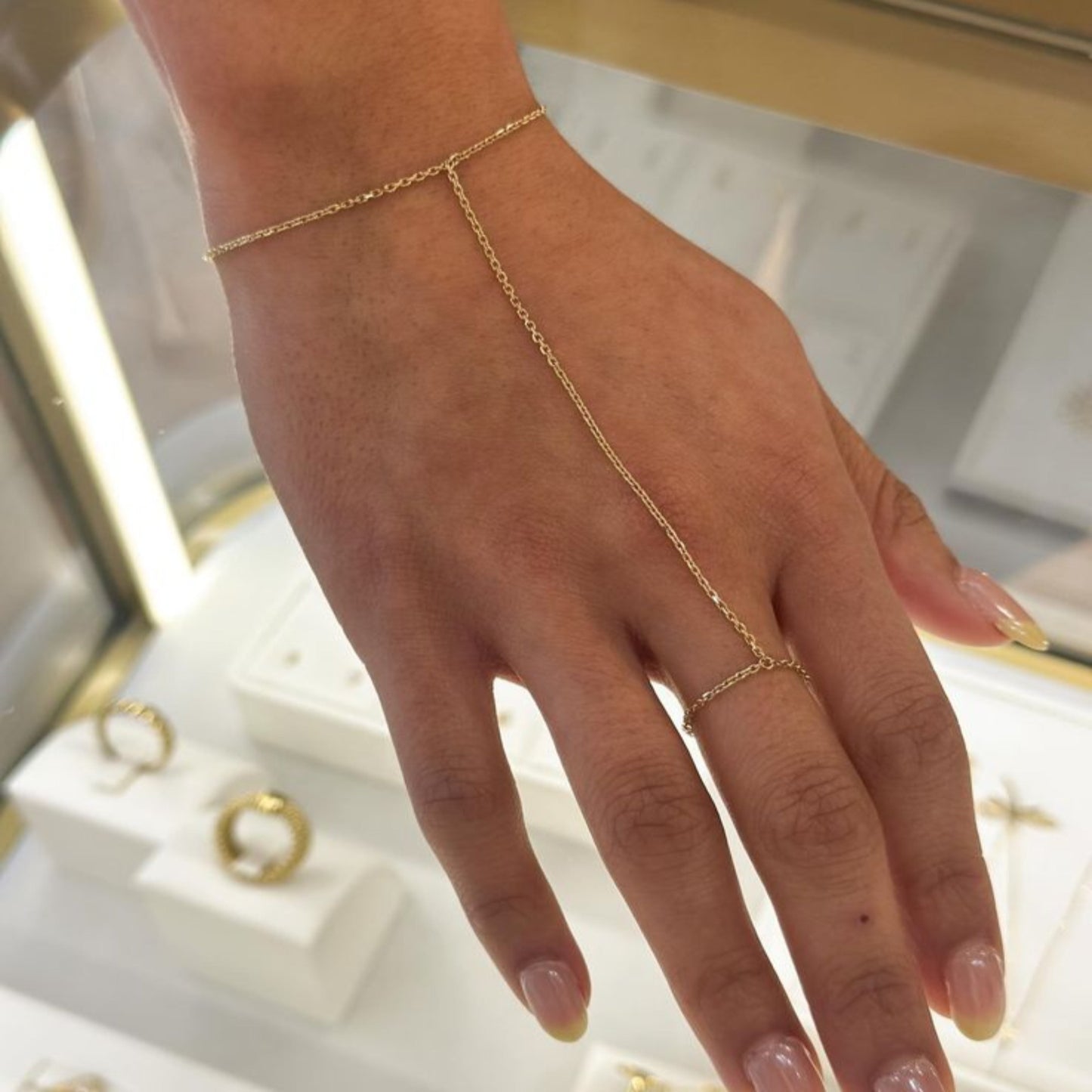 Gold hand chain and ring on a hand with a blurred jewelry box background