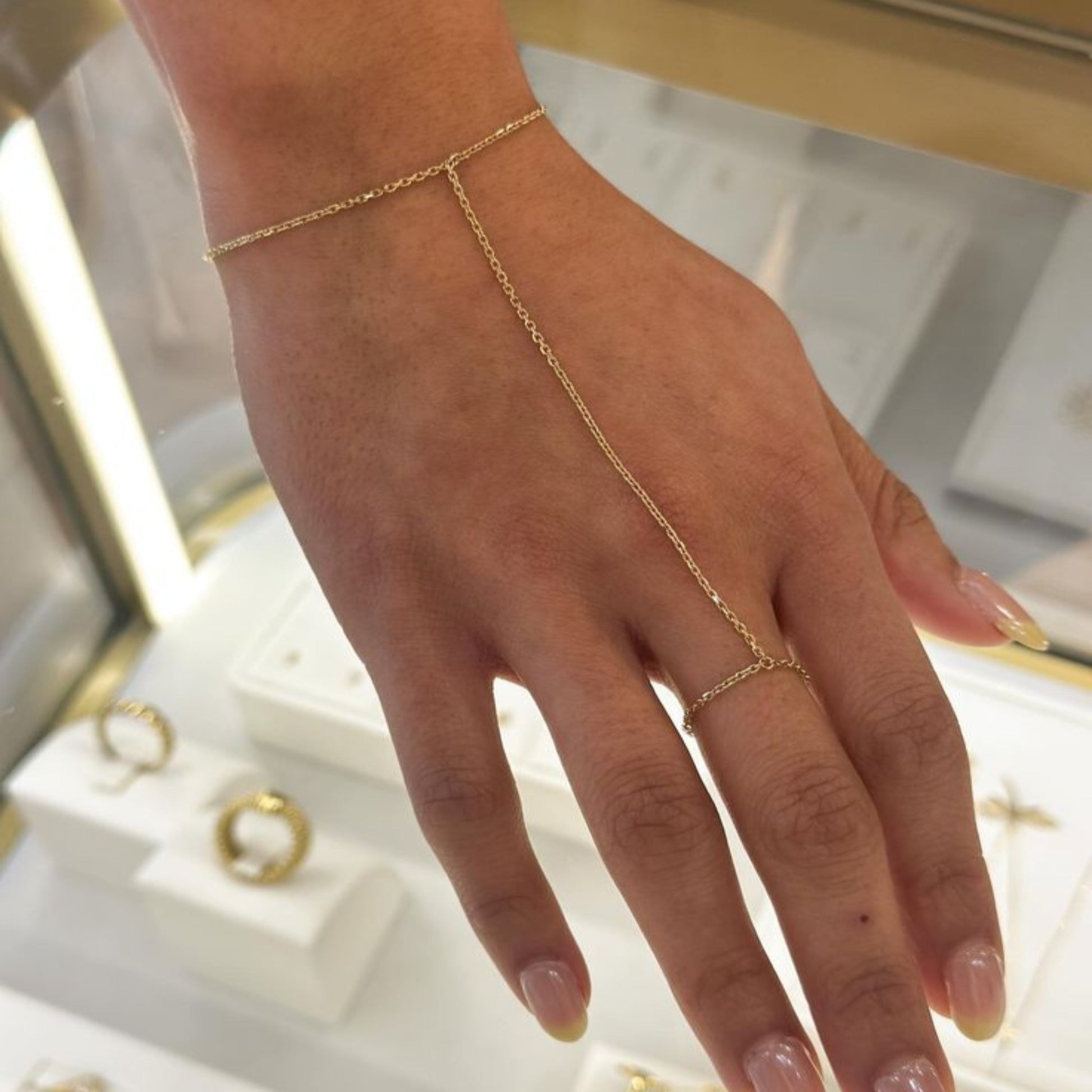Gold hand chain and ring on a hand with a blurred jewelry box background