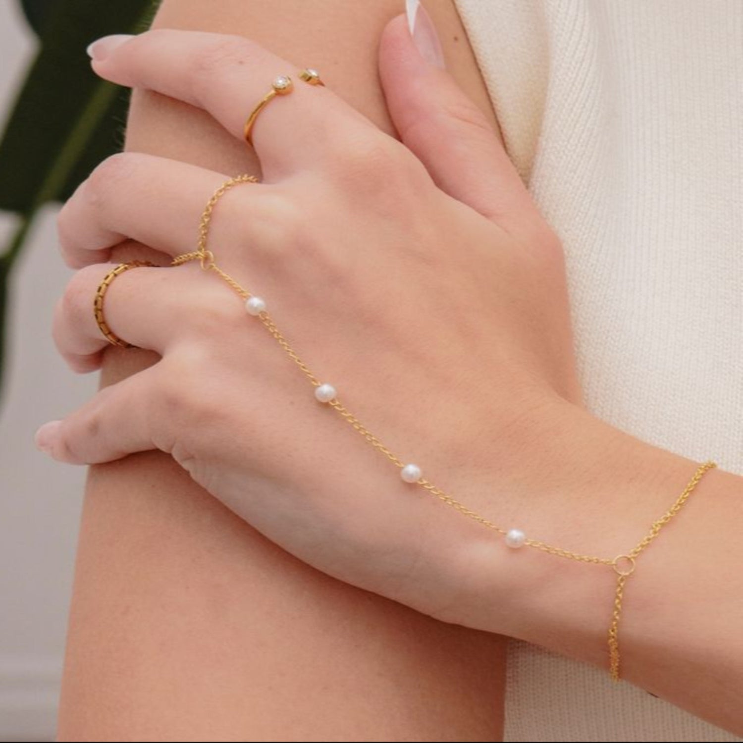 Gold bracelet with pearls on a hand against a neutral background