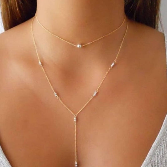 Gold necklace with small beads on a person wearing a gray top.