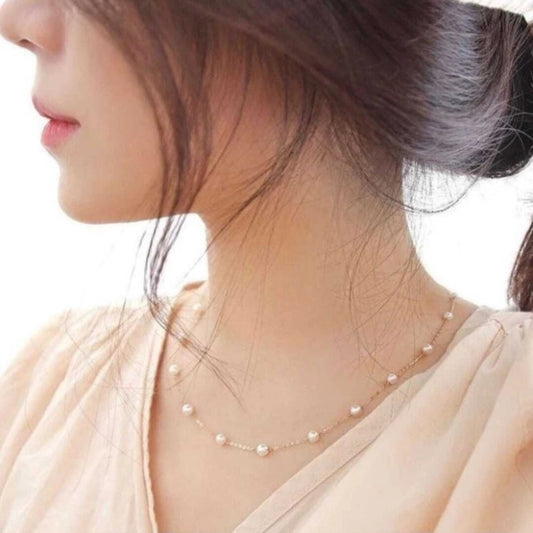 Close-up of a woman wearing a delicate pearl necklace against a neutral background