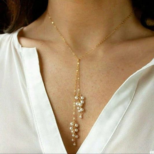 Gold necklace with pearl drops worn by a person in a white shirt