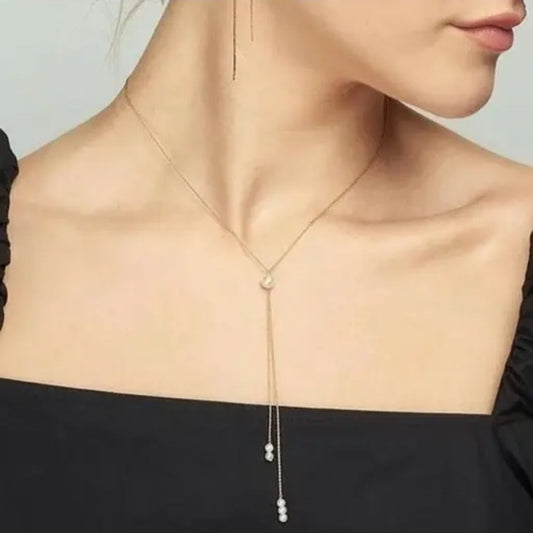 Necklace with pearl drops worn by a person against a neutral background