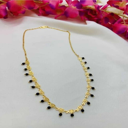 Gold necklace with black beads on a white surface with pink flowers in the background