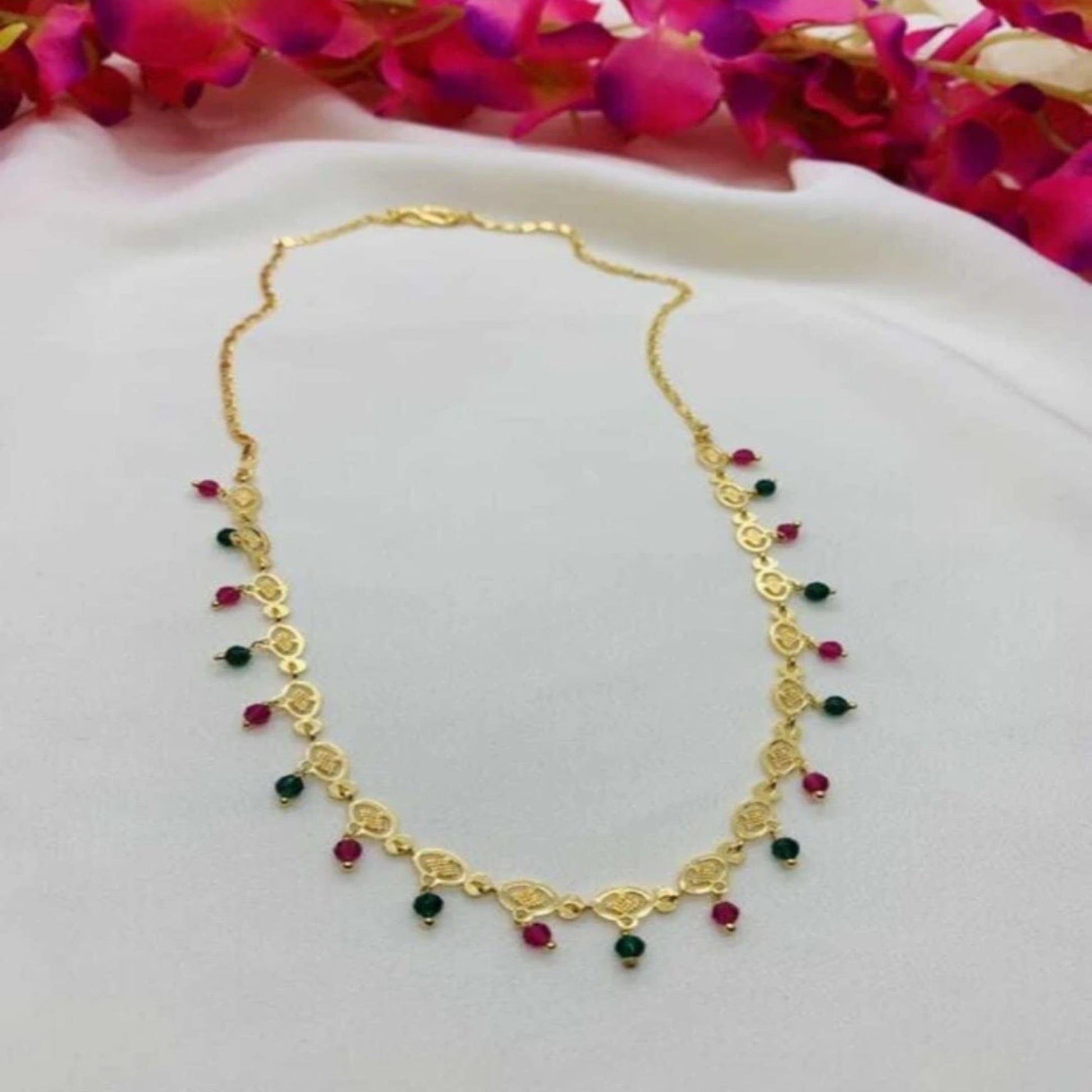 Gold necklace with red and green beads on a white background