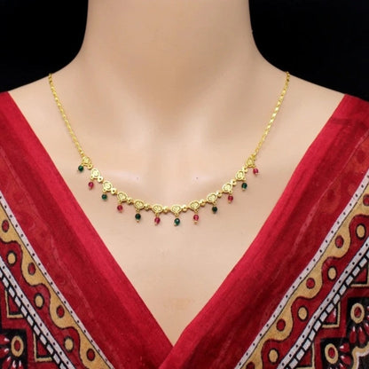 Gold necklace with red and green beads on a mannequin wearing a red saree.