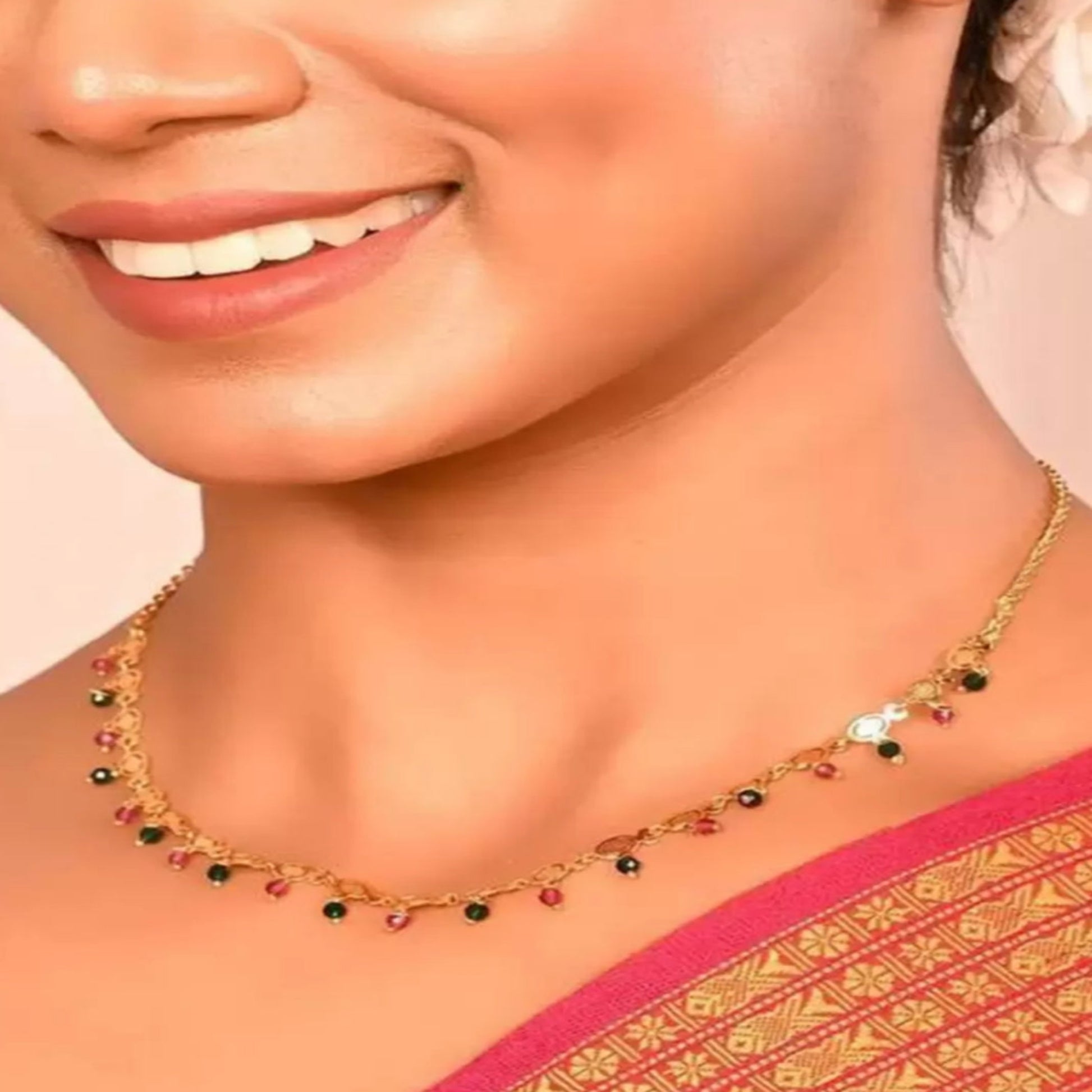 Woman wearing a gold necklace with gemstones on a pink and gold saree.