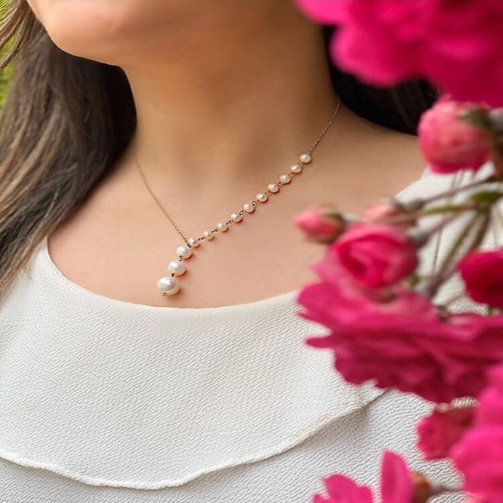 Pearl necklace worn by a person with pink flowers in the foreground