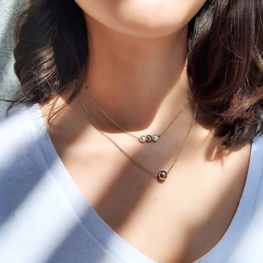 Close-up of a necklace with small beads on a person wearing a white top.