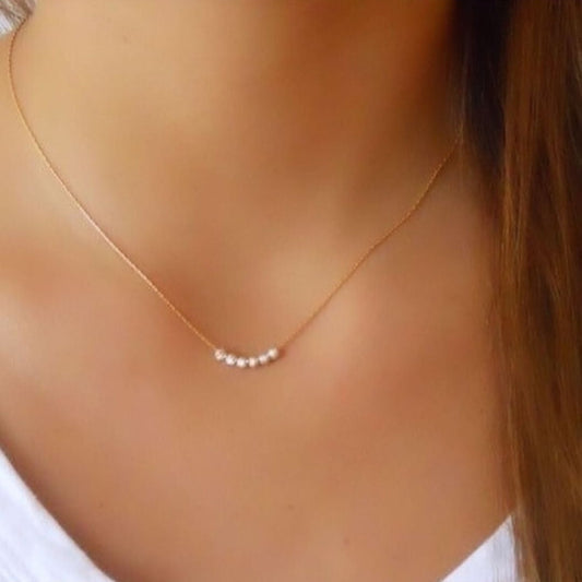 Gold necklace with small pearls on a person wearing a white top