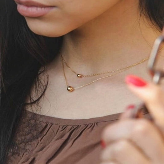Close-up of a person wearing a gold necklace with small round pendants.