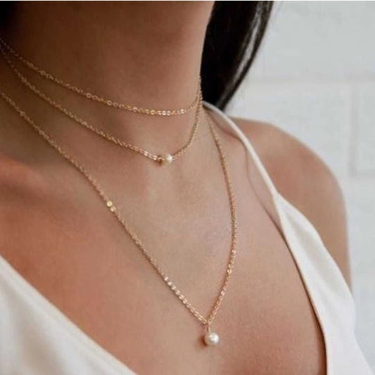 gold necklaces with pearl pendants on a person wearing a white top.