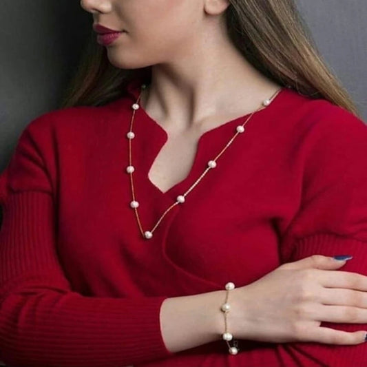 Woman wearing a red sweater and pearl necklace and bracelet against a gray background