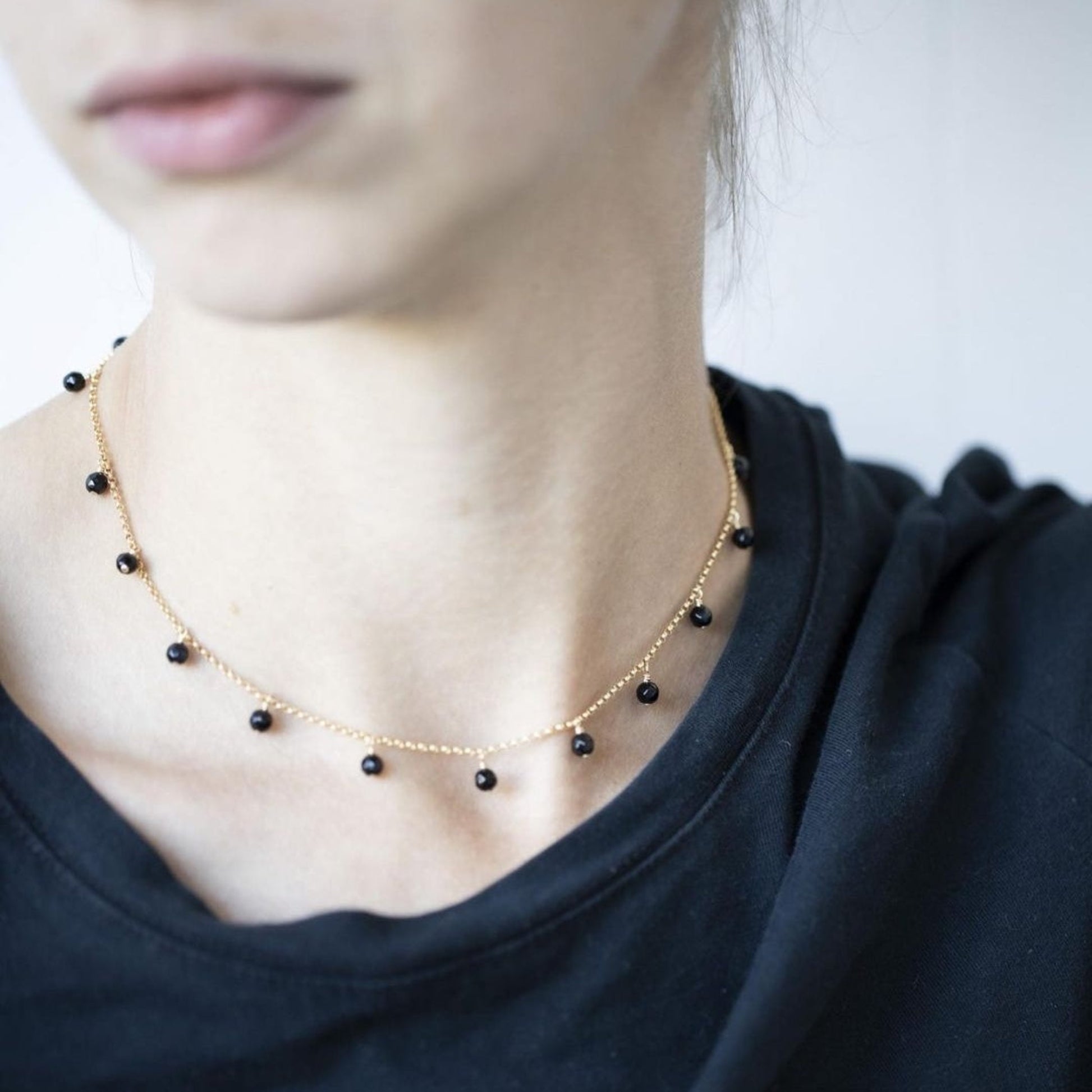 Necklace with black beads worn by a person against a neutral background