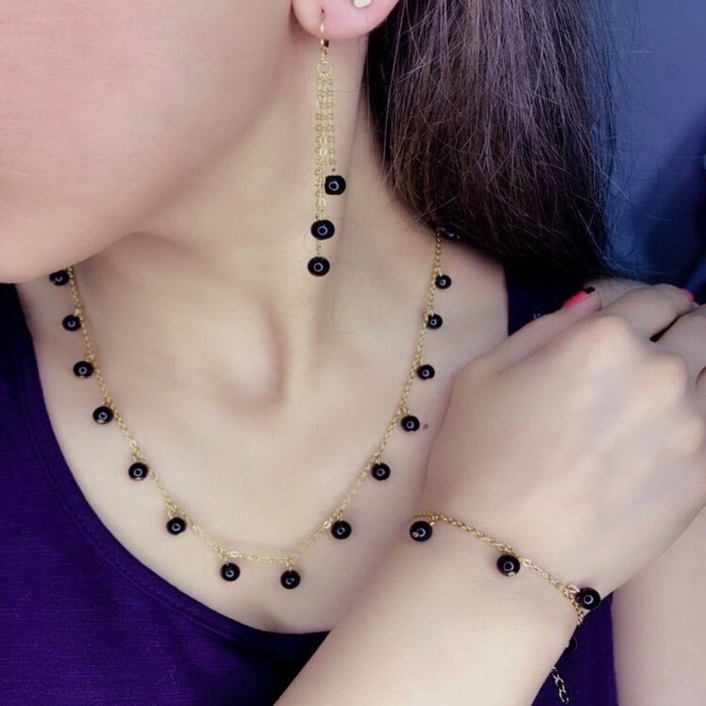 Person wearing a gold necklace with black beads and matching earrings.