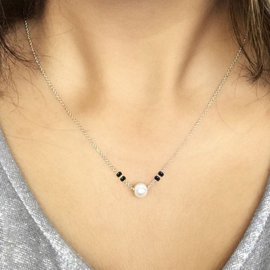 Necklace with a pearl pendant on a person wearing a silver top.