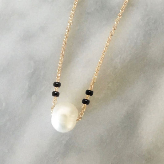Necklace with a large pearl pendant and black beads on a light gray background