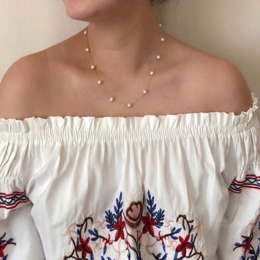 White off-shoulder top with colorful embroidery and pearl necklace.