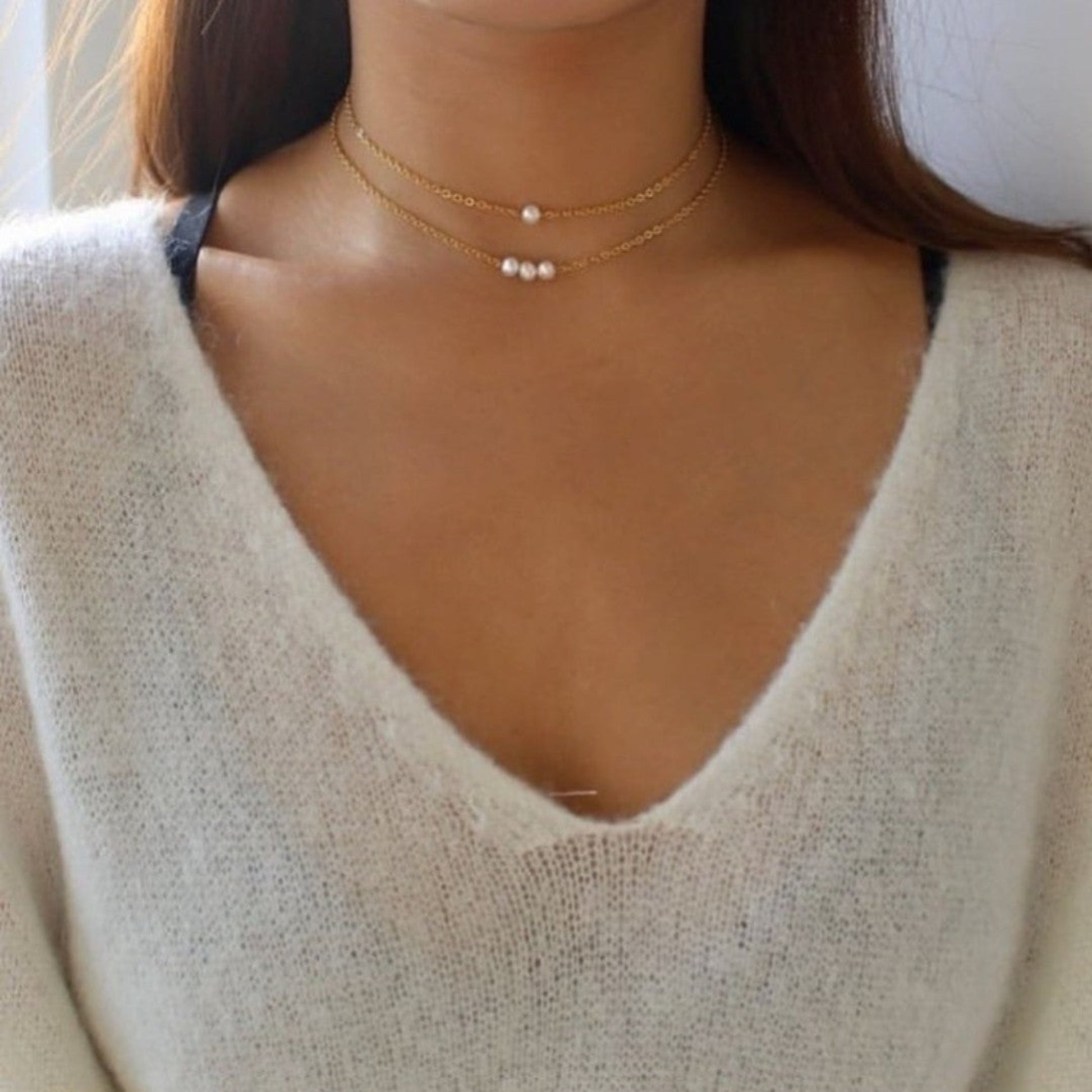 Close-up of a person wearing a delicate gold necklace with small beads.