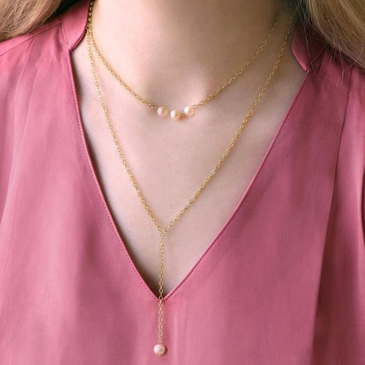 Gold necklaces with pearl pendants on a pink blouse