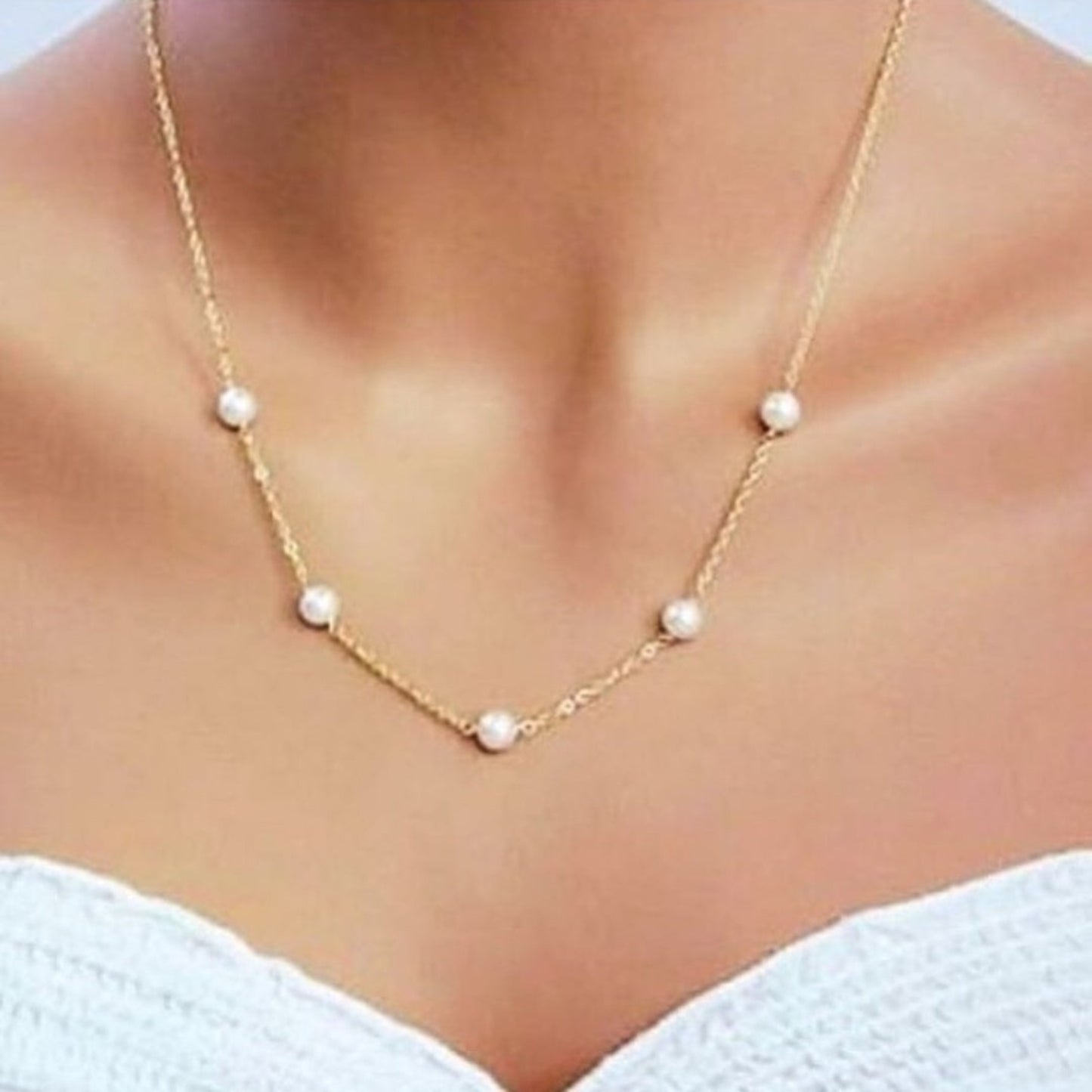 Gold necklace with pearls on a person wearing a white top