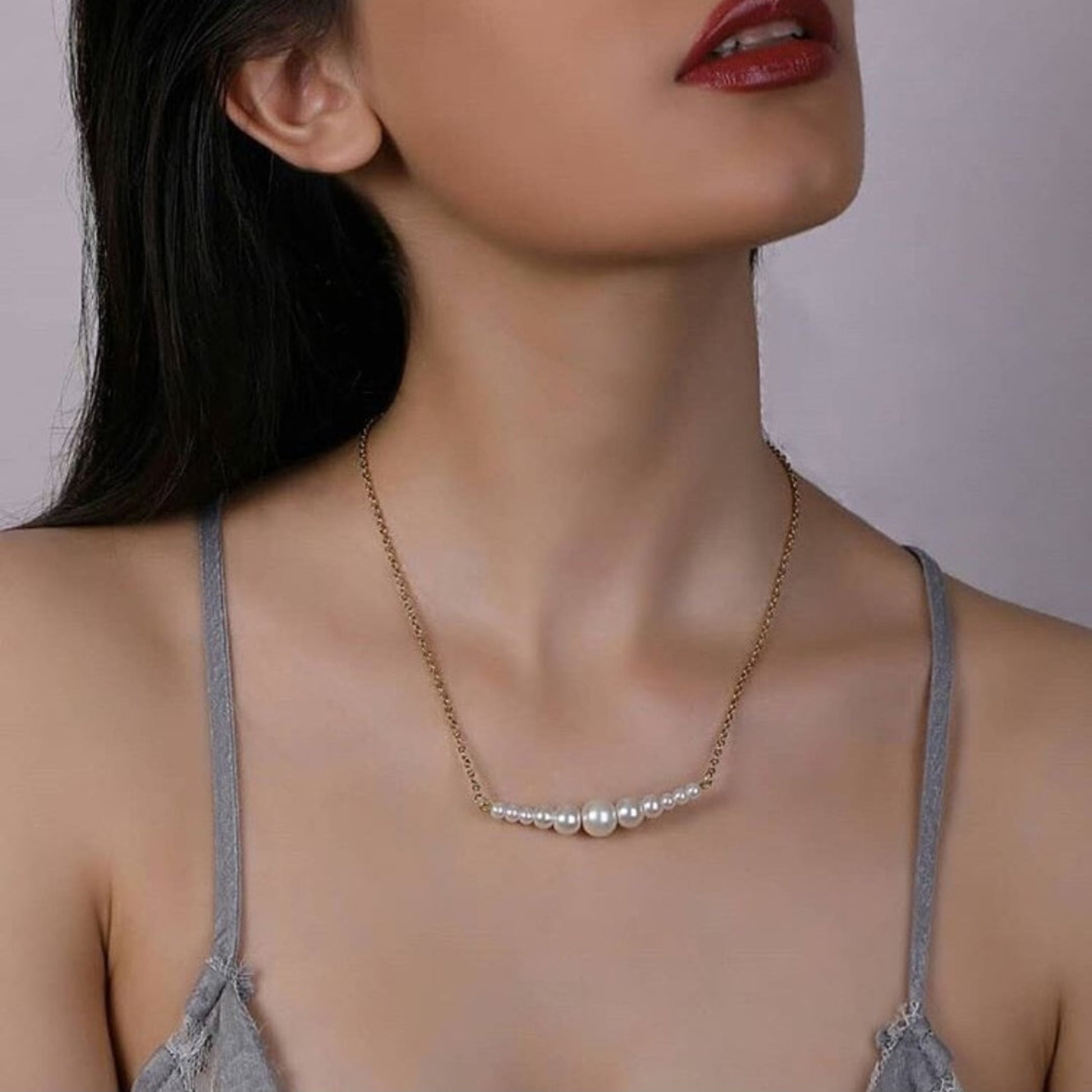 Woman wearing a delicate necklace with a plain background