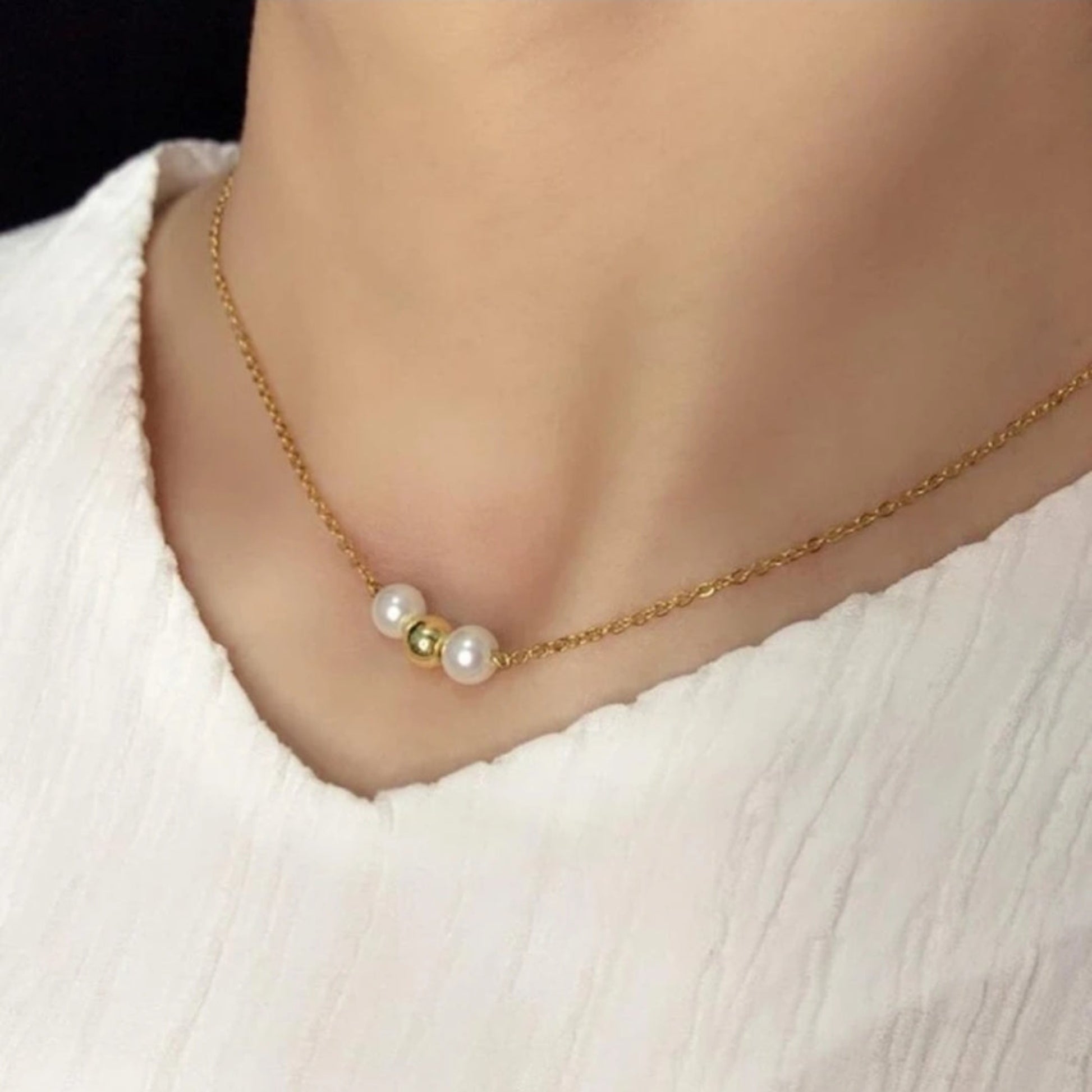 Gold necklace with pearls worn by a person on a plain background