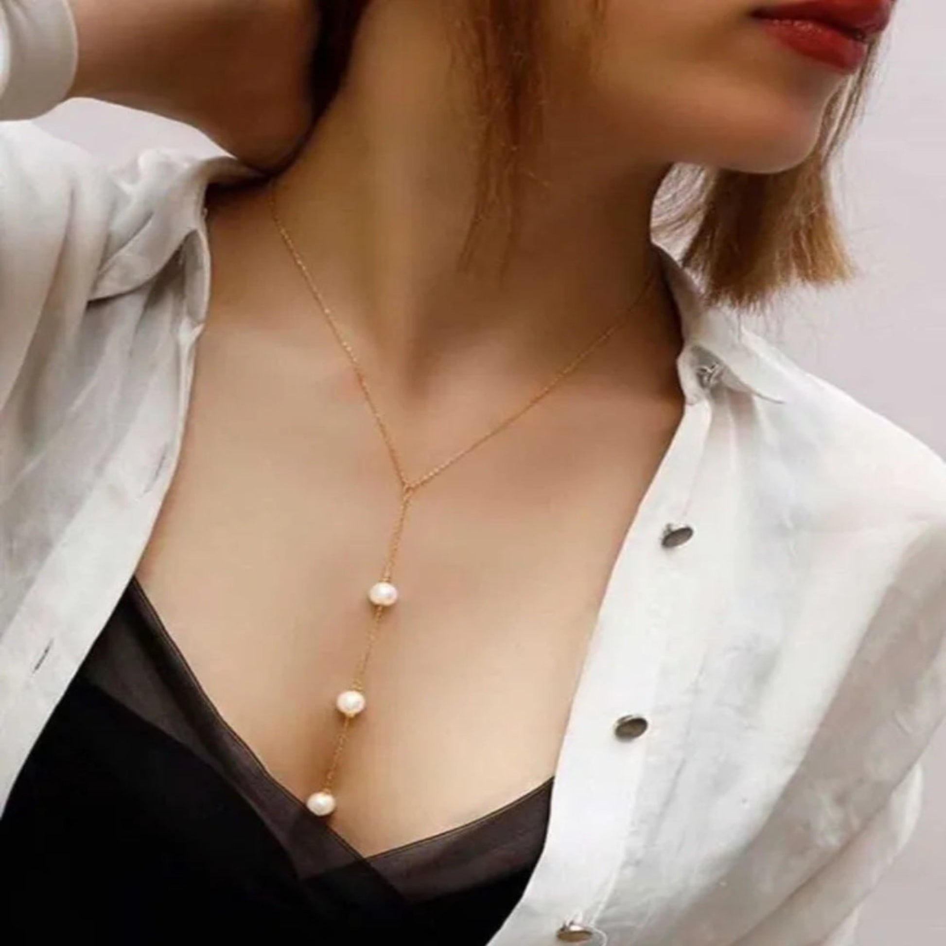 Person wearing a gold necklace with pearls, partially visible outfit