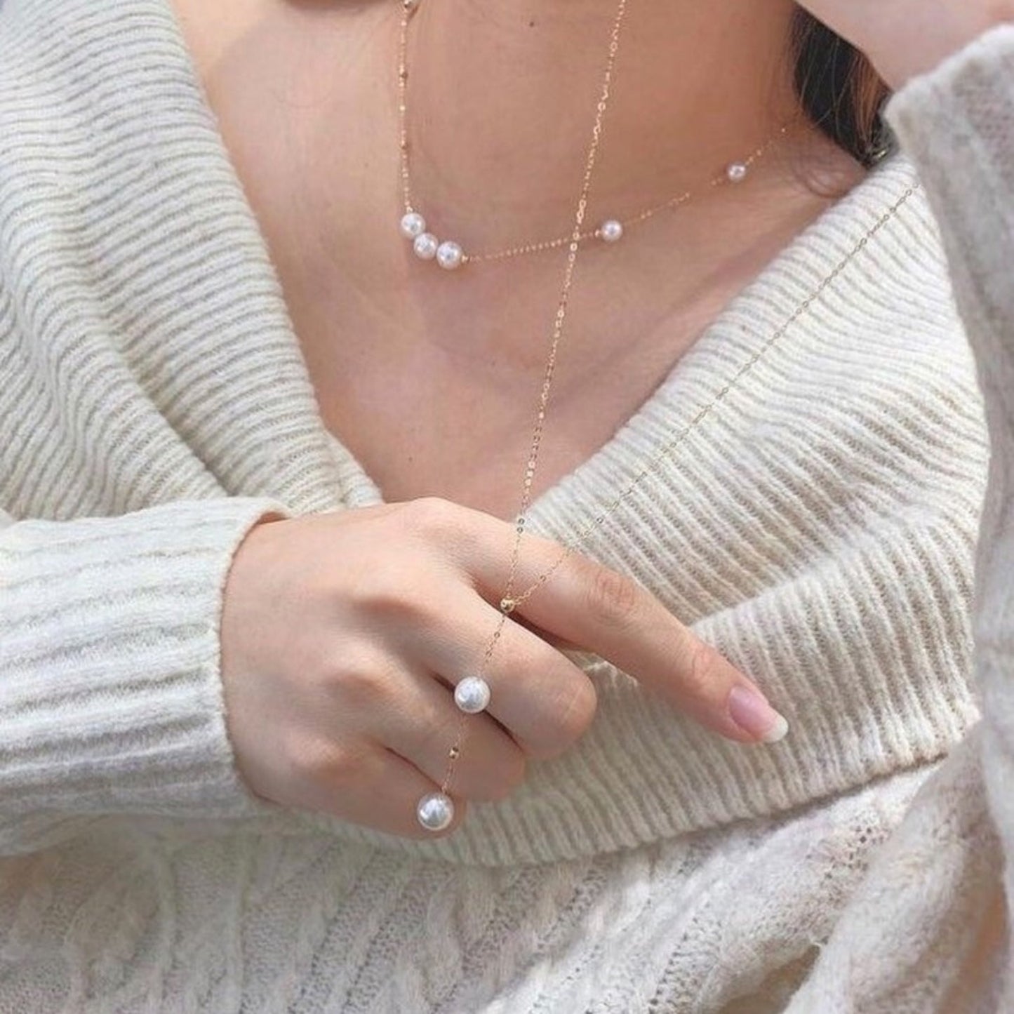 Person wearing a delicate pearl necklace and ring with a neutral background