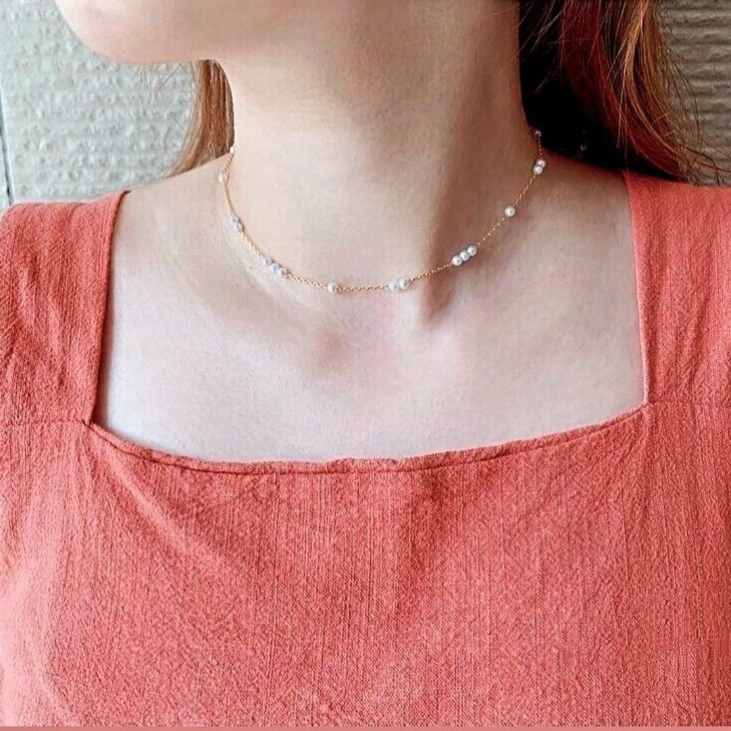 Person wearing a delicate pearl necklace with a plain background