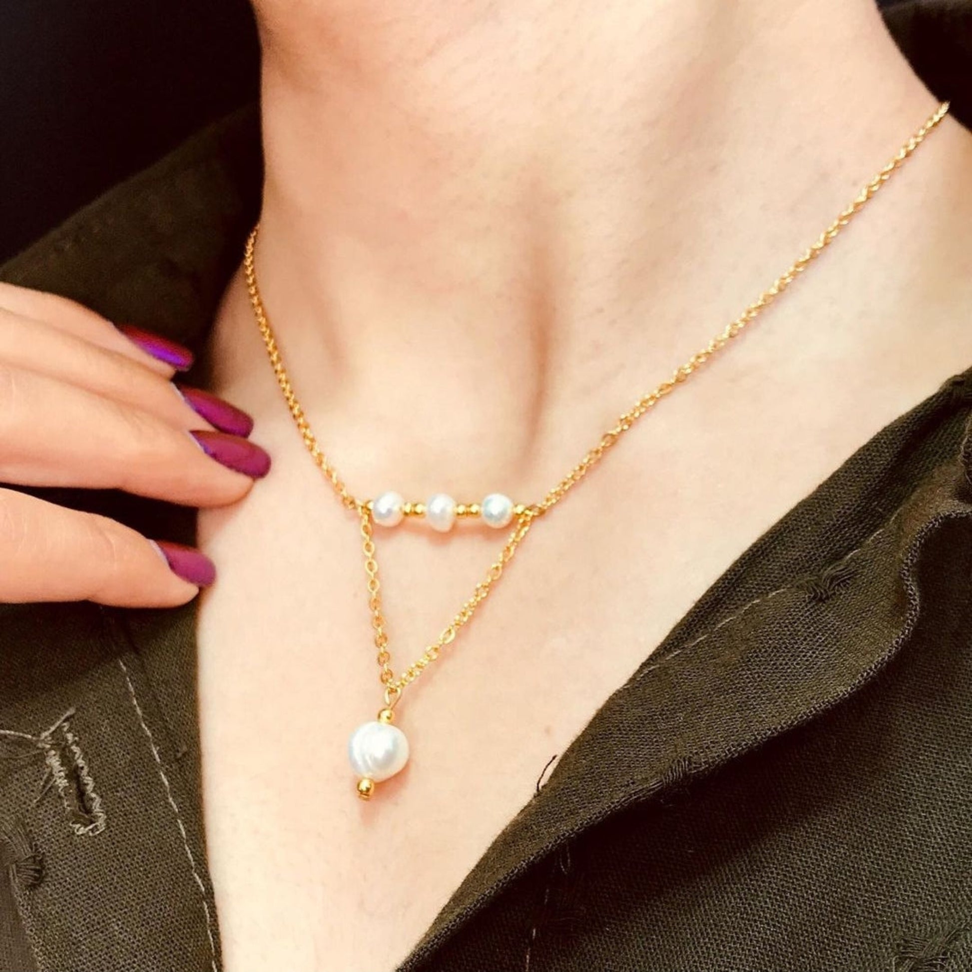 Gold necklace with pearl pendants worn by a person, with a hand adjusting the necklace.